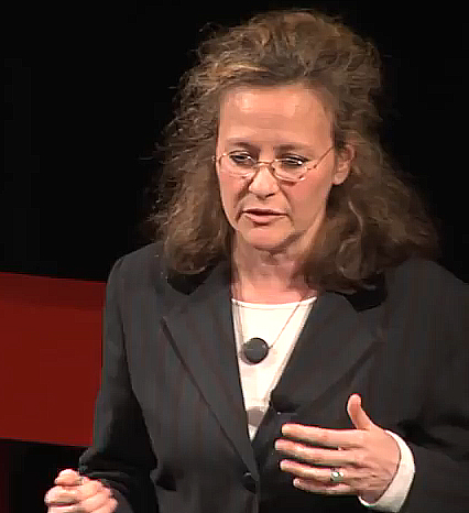 Lesli Bisgould gives a lecture. She is wearing a suit jacket, a white blouse and glasses.